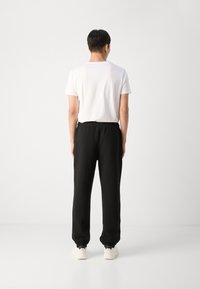 Pantalons de survêtement noirs avec des poignets élastiques et une taille ajustable, associés à un t-shirt blanc uni. Design épuré et minimal.