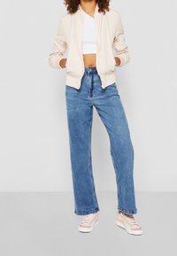 Ljusrosa bomberjacka, vit crop top, blå vida jeans och flerfärgade låga sneakers med pastelliga accenter. Släta tyger och avslappnad passform.