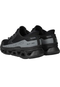 Scarpe slip-on nere Skechers con parte superiore in rete, suola spessa nera e dettagli grigi. Presenta un design a punta rotonda e dettagli texture.