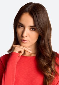 Langärmliges rotes Oberteil aus dünnem, strukturiertem Stoff, mit rundem Halsausschnitt und taillierter Silhouette, längeren Bündchen und subtilen Stitching-Details.
