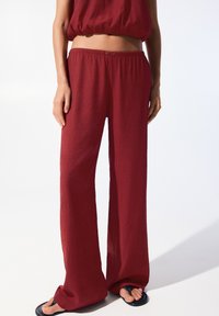 Luftiga, röda byxor i textil med avslappnad passform och elastisk midja. Bärs med svarta flip-flops.
