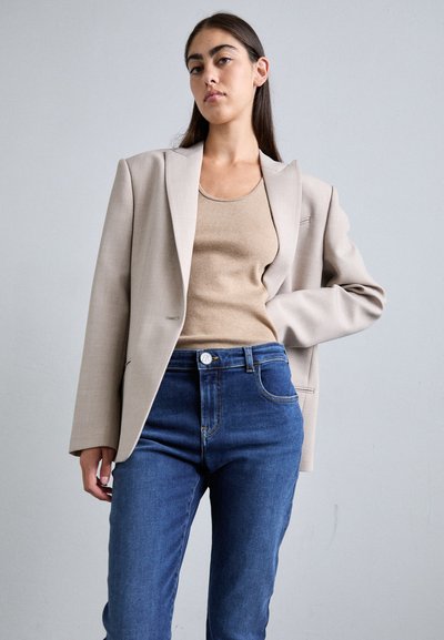 Μπεζ σακάκι με διαρθρωτούς ώμους και πέτο, φορεμένο πάνω από ταμπά ριπτομπλούζα. Συνδυασμένο με σκούρα μπλε ψηλόμεσα τζιν.