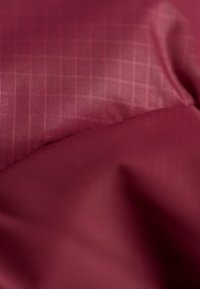 Tessuto texturizzato in bordeaux con un sottile motivo a rete, che mostra sezioni lisce e stropicciate e riflessi di luce variabili.