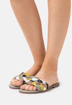 Sandalias deslizables tejidas con tiras multicolores en verde, amarillo, negro y blanco; suela plana con superficie texturizada.