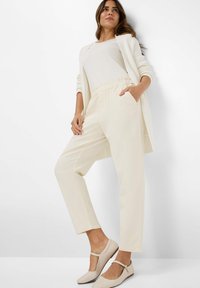 Crème-kleurige elastische taillebroek met zijzakken, gecombineerd met een wit top en beige T-sandalen. Gladde textuur, relaxed fit.