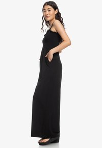 Black maxi dress with a smocked bodice, thin straps, and pockets. It features a flowing design and soft, lightweight fabric.