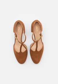 Scarpe con tacco in suede marrone con design a T-strap, intagli circolari e accessori in oro. Interno liscio con plantare imbottito.