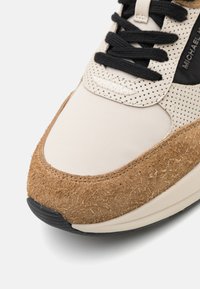 Sneaker color sabbia e beige con tomaia in suede testurizzato, dettagli perforati beige, lacci neri e suola nera.