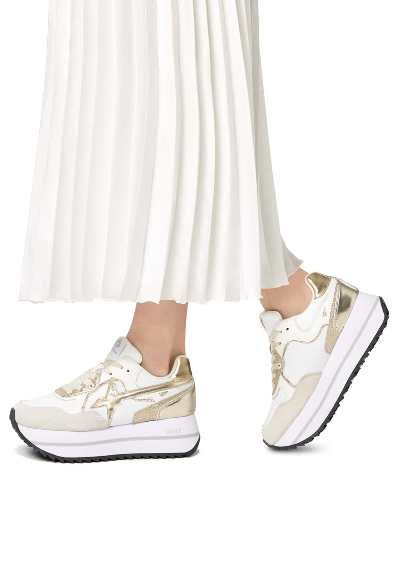 Vita sneakers med guld accenter, med en texturerad ovandel, lagerdesign och en tjock vit sula med ett svart mönster.