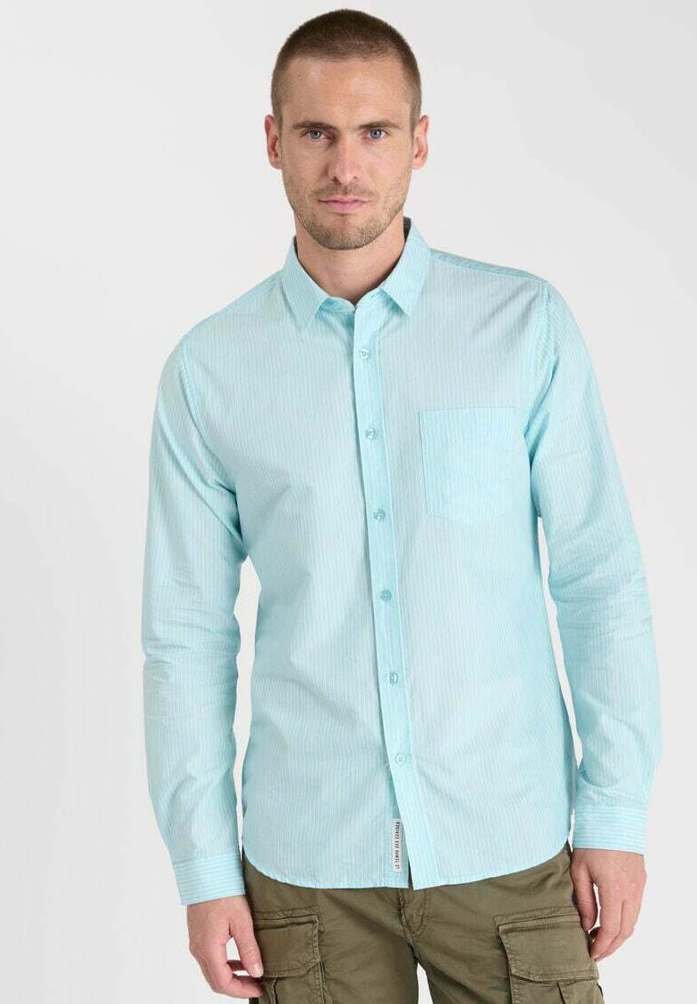 Chemise à rayures bleu clair avec boutons, à manches longues, une poche poitrine unique et un ourlet arrondi. Fabriquée en tissu lisse avec une légère brillance.