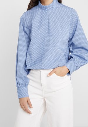 Lichtblauw geruit blouse met hoge kraag, ontspannen pasvorm, lange mouwen met elastische manchetten, gedragen met witte broek. Voorzien van lichtgewicht stof.