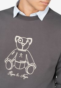 Grijze sweatshirt met een textuurafwerking, voorzien van een witte geborduurde teddybeerontwerp aan de voorkant en de tekst "Harper & Meyer" eronder.