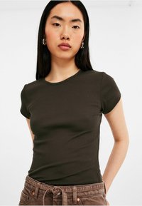 T-shirt ajusté de couleur vert olive foncé, à manches courtes et texture côtelée. L'encolure est ronde, et le tissu semble doux et lisse.