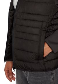Gilet imbottito nero con chiusura a zip, caratterizzato da una texture trapuntata, tasche laterali e fodera interna a contrasto. Materiale morbido e leggero.