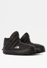 Pantuflas negras acolchadas con un alto cuello, suela de goma y detalle del logo blanco en el lateral. La textura suave y la forma redondeada ofrecen comodidad.