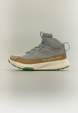 Helehall ja pruun keskmise kõrgusega matkajalats roheliste paeltega, tekstuurse beežse tallaga, sinise tõmblukuga ja küljele trükitud "THE NORTH FACE" tekstiga.