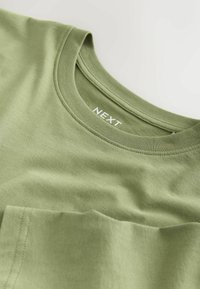 Pamucna majica maslinasto zelene boje, okrugli izrez, kratki rukavi, s malim džepom na prsima, ravnim šavovima i mekanom teksturom.