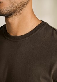 Brun crewneck t-shirt med en glat tekstur og syet hals. Nærbillede fremhæver stoffets blødhed og pasform.