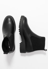 Botas negras hasta los tobillos con upper de cuero liso, paneles de tela acanalada, tira para tirar y una suela de goma resistente con agarre texturizado.