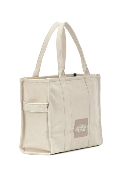 Saco de canvas bege com alças duplas superiores, fecho em zip, bolso lateral e um logótipo na frente. Forma quadrada e design estruturado.