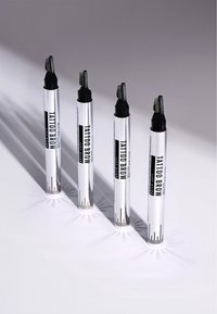 Four silver Maybelline Tattoo Brow Lift Stick tubes with angled black comb applicators casting long shadows on a light surface.