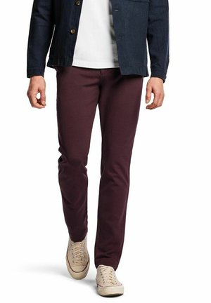 Bordeauxrode broek in een slim fit ontwerp met een gladde textuur, gecombineerd met beige sneakers en een donkerblauw jasje.