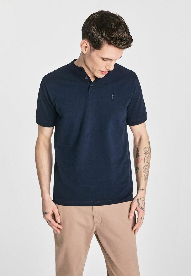 Granatowa koszulka polo z dwoma guzikami przy kołnierzyku oraz małym haftowanym logo na lewej piersi. Krótkie rękawy i miękka, gładka tkanina.