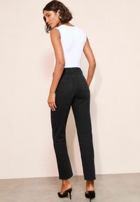 Černé džíny s vysokým pasem a fitted siluetou, vyrobené z denimu, s zadními kapsami a čistým lemem. Kombinované s bílým body.