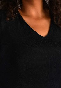 Top negro de cuello en V confeccionado con un material texturizado que tiene un brillo sutil. Vista en primer plano del escote, sin patrones ni elementos metálicos visibles.