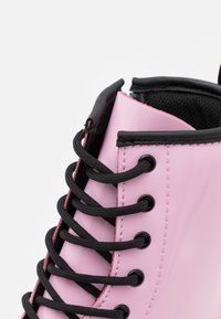 Sneaker in pelle lucida rosa con lacci neri, dotata di occhielli neri e colletto imbottito per il comfort. Superficie texture per una migliore aderenza.