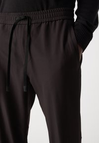 Pantalonii sport negri au un sistem de talie elastică cu şnur, buzunare laterale și o textură netedă. Designul este conic.