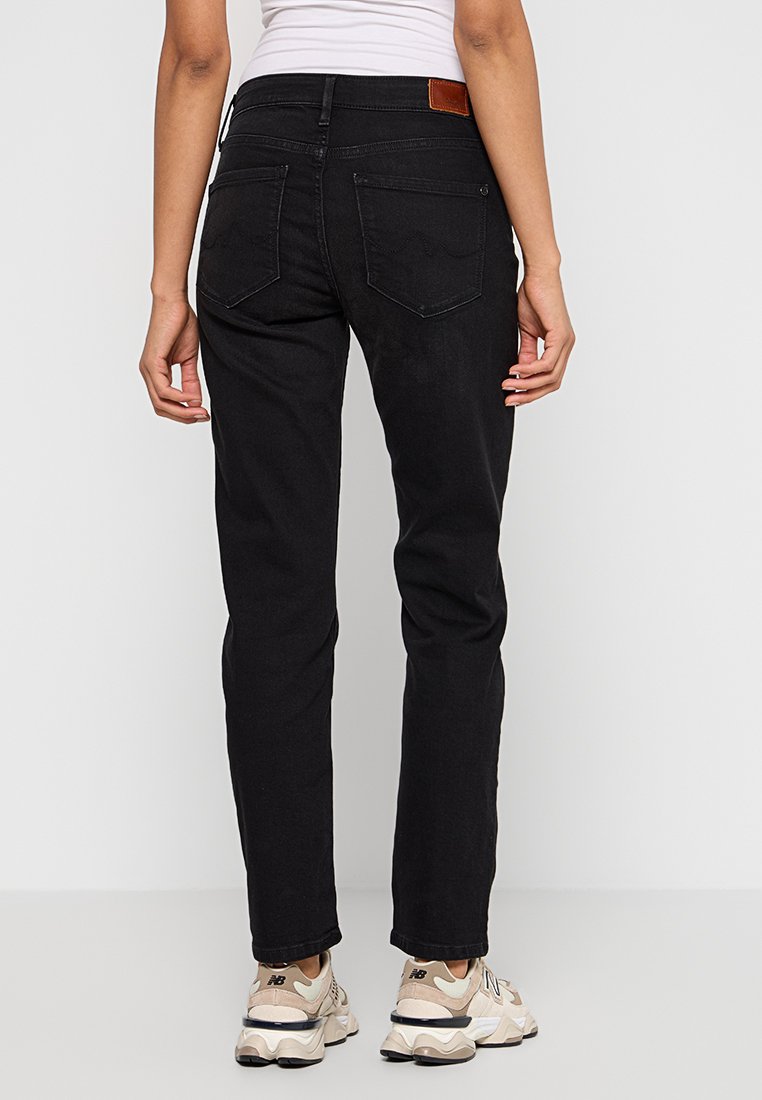 Jean en denim noir avec une coupe slim, comprenant deux poches arrière, une étiquette en cuir marron sur la ceinture et des détails d'ourlet effilochés.
