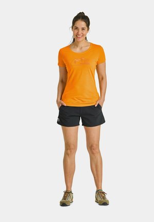 Orange short-sleeve shirt with a mountain graphic, paired with black shorts. Model wears light brown shoes with dark soles.