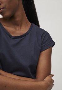 Granatowa koszulka z okrągłym dekoltem i podwiniętymi krótkimi rękawami. Gładki materiał o luźnym kroju. Posiada prosty, nieozdobiony design.