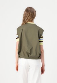 Ärmelloses Oberteil in Olivgrün mit farblich abgesetzten, gestreiften kurzen Ärmeln, lockerem Schnitt und gerafftem Rückendetail.