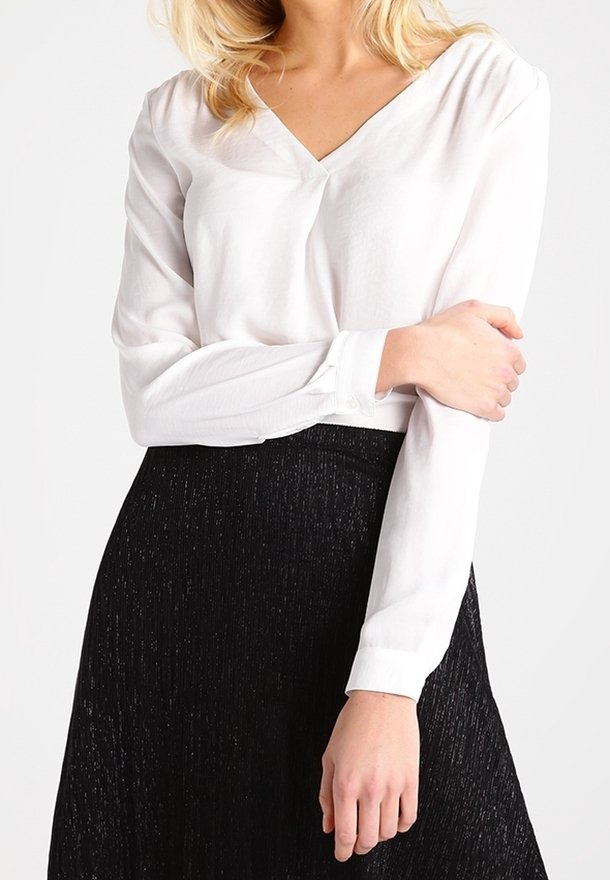 Blouse blanche à manches longues avec un col en V et des poignets boutonnés. Associée à une jupe évasée noire, texturée, avec un léger éclat.