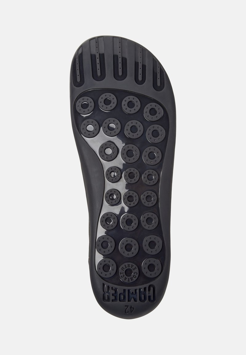 Black rubber sole with circular tread pattern and drainage holes, featuring a raised logo near the heel, designed for grip and water drainage.