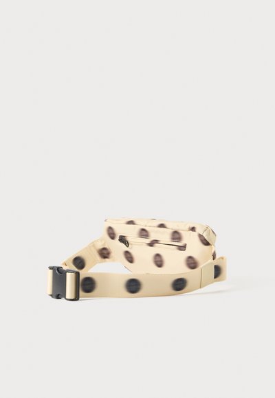 Banane beige à pois noirs, poche zippée à l'avant et sangle réglable avec boucle en plastique.