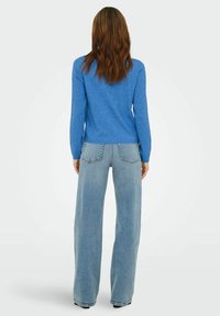 Blå genser med lange ermer og avrundet kant, kombinert med lyseblå vide jeans med baklommer og teksturert overflate.