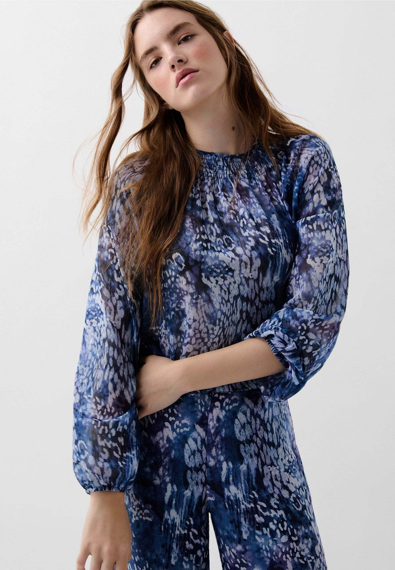 Long-sleeve blue and purple patterned blouse with a gathered neckline and elastic cuffs, featuring a soft, textured fabric.