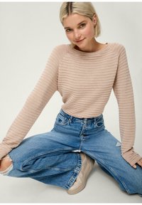 Maglione a maniche lunghe beige a coste abbinato a jeans in denim azzurri a gamba larga. L'outfit presenta una vestibilità rilassata e dettagli di cucitura visibili.