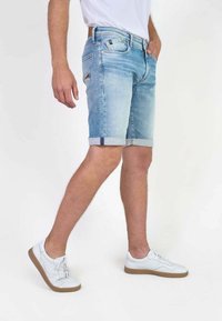 Shorts de mezclilla azul claro con dobladillos enrollados, con un diseño clásico de cinco bolsillos y un ligero desvanecimiento. Combinados con zapatillas blancas.