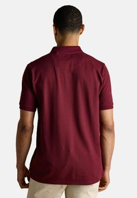 Burgundi värvi lühikeste varrukatega polo särk, klassikalise krae ja veidi tekstureeritud viimistlusega. Omab sirget tagumist äärt ja külgavaid avasid.