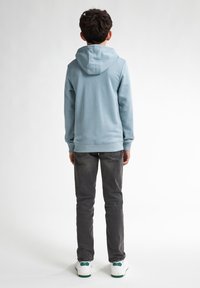 Ljusblå hoodie med kenguruficka och dragsnöre, i kombination med grå jeans och vita sneakers med gröna detaljer.