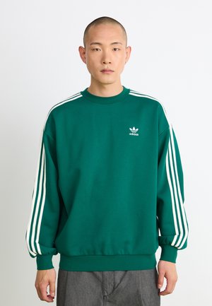 Green sweatshirt with white triple stripes on sleeves, ribbed crew neck, and elastic cuffs. Small white adidas logo on chest.