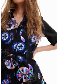Czarna sukienka koszulowa z kolorowymi okrągłymi wzorami w odcieniach niebieskiego, różowego i zielonego. Zawiera pasek oraz krótkie rękawy z zapięciem na guziki.