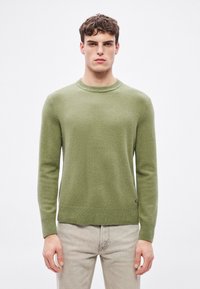 Zöld gyapjú pulóver kerek nyakkivágással, hosszú ujjakkal, bordázott mandzsettákkal és szegéllyel. Puha tapintású, testhezálló fazonú.