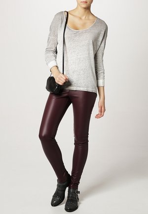 Grauer Langarm-Oberteil, bordeauxrote Kunstleder-Leggings, schwarze Nieten-Stiefeletten und eine kleine schwarze Umhängetasche.