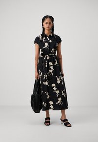 Melnas ziedu kleitas izgatavota no gludas auduma, ar īsām piedurknēm, pieguļošu jostu un plūstošu svārku. Pieveids ar melnu somu un sandālēm.