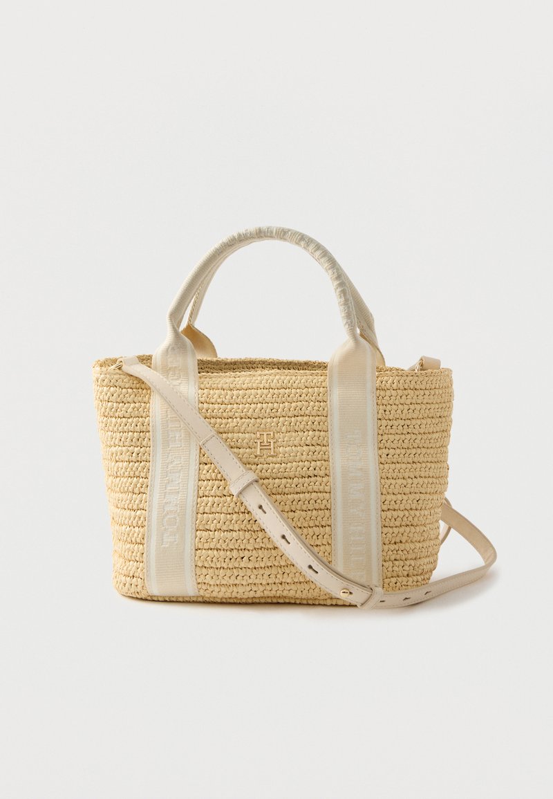 Geflochtene Strohtasche in hellem Beige mit strukturierter Form. Verfügt über cremefarbene Träger und ein goldenes Logo-Detail auf der Vorderseite. Verstellbarer Gurt inklusive.
